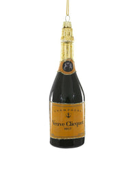 The Cody Foster Champagne Brut Ornament is a hand-crafted hanging decoration shaped like a Veuve Clicquot-style champagne bottle, featuring a gold foil top and orange label, shown against a white background.