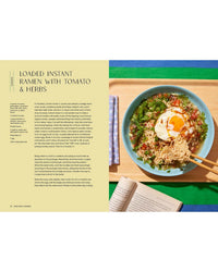 Enjoy a comforting meal from Snacking Dinners by Chronicle Books: instant ramen with a fried egg, tomatoes, and herbs on a green plate with chopsticks. An open book and striped napkin rest nearby on a blue surface under bright light.