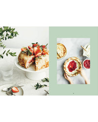 Inspired by Finnish recipes from Cozy Publishing’s "Cookbook: Crumbs of Joy," a layered crepe cake with strawberries is shown on a white stand, while hands assemble it with crepes, cream, and strawberry filling nearby.