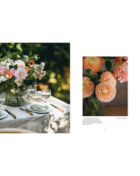 A table set with plates, cutlery, glasses, and a large vase of pink and peach dahlias displays the natural bouquets featured in "Where Flowers Bloom" by Cozy Publishing, shown in bright natural light with orange dahlias close-up.