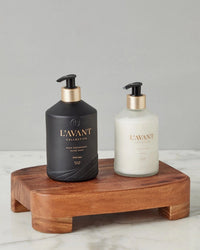 Two pump bottles, one black (hand soap) and one white (lotion), labeled LAVANT Collective, rest on the etúHOME New Classic Rectangle Trivet Riser, Small, atop a marble surface—a chic kitchen essential.