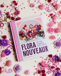 The book "Flora Nouveaux" by Chronicle Books rests on a surface adorned with vibrant modern dried flowers in pink, purple, and fuchsia hues.