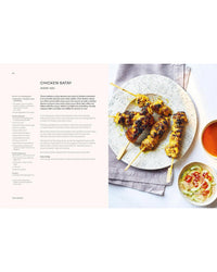 A plate of grilled chicken satay skewers with herbs, dipping sauce, and cucumber salad sits on a light cloth. Recipe text from "Thai Made Easy" by Chronicle Books is shown on the left—ideal for lovers of authentic Thai cuisine.