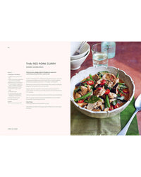 A bowl of Thai red pork curry with sliced pork, green beans, and red chilies rests beside a spoon, two water glasses, and stacked plates. The "Thai Made Easy" cookbook by Chronicle Books is displayed on the left.