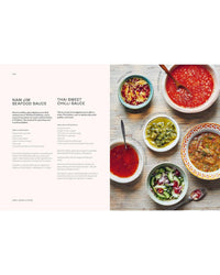 An overhead view of six colorful bowls with Thai sauces and relishes, some with spoons, on a light tabletop next to an open page from "Thai Made Easy" by Chronicle Books, featuring nam jim seafood and sweet chilli sauce recipes.
