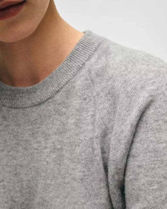 A close-up shows a person wearing the White + Warren Cashmere Easy Sweatshirt in Grey Heather. Only the lower face, neck, and upper chest are visible against a plain, neutral background.