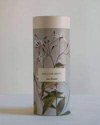 A cylindrical container labeled "Mellow Mint Tea Gift Set" by The Quiet Botanist, adorned with floral and leaf illustrations—ideal for herbal or peppermint tea—set against a simple light background.