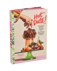 Hot Date! by Chronicle Books is a cookbook with date-focused recipes. Its cover features a hand with dates over a dish of dates, grapes, and cherries, plus pomegranate and figs below—a nod to Middle Eastern cuisine and this ancient superfood.