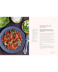 A gray plate with spicy pork and chili dip garnished with cilantro sits among fresh veggies—a perfect scene for fans of easy Thai cooking, inspired by "Thai Made Easy" from Chronicle Books.