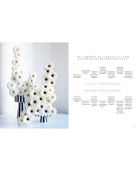 A modern floral arrangement of tall white flowers in striped vases sits beside "The Flower School" by Chronicle Books, a text exploring classical and contemporary proportions in floral design.