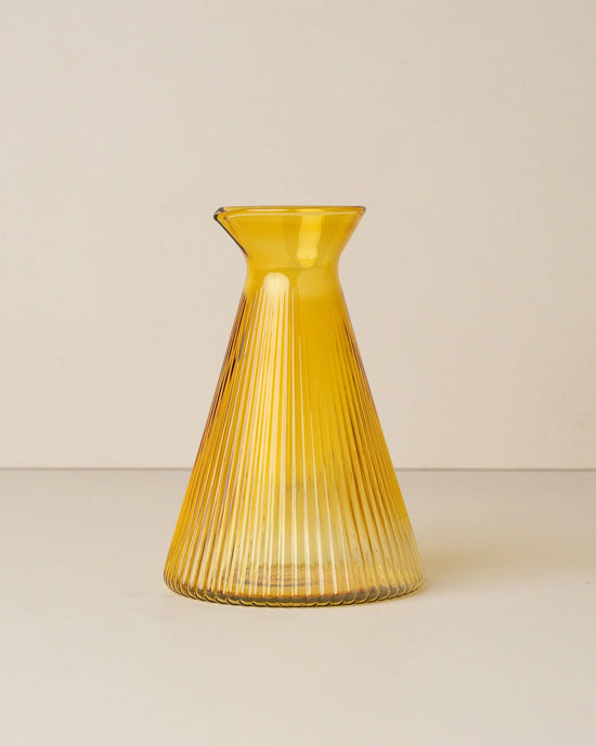 The Saarde Kairos Angular Carafe in Yellow Topaz features ribbed, durable borosilicate glass with a narrow neck and flared rim, shown against a plain, light background.