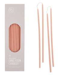 A box of The Floral Society's Beeswax Long Stem Candles contains slim, pink tapers; three matching candles are shown outside the box, emphasizing their elegant, elongated form.