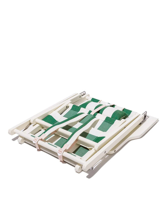 The Tommy Chair - Acacia White - Crew Canyon Green Stripe by Business & Pleasure Co features a compact, foldable design with green and pink woven straps, showcased on a white surface for easy portability.