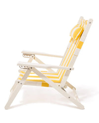The Tommy Chair - Acacia White - Crew Mimosa Yellow Stripe by Business & Pleasure Co is a white folding reclining beach chair with yellow and white striped UV-resistant canvas, armrests, and a matching pillow. Shown from the side on a white background.