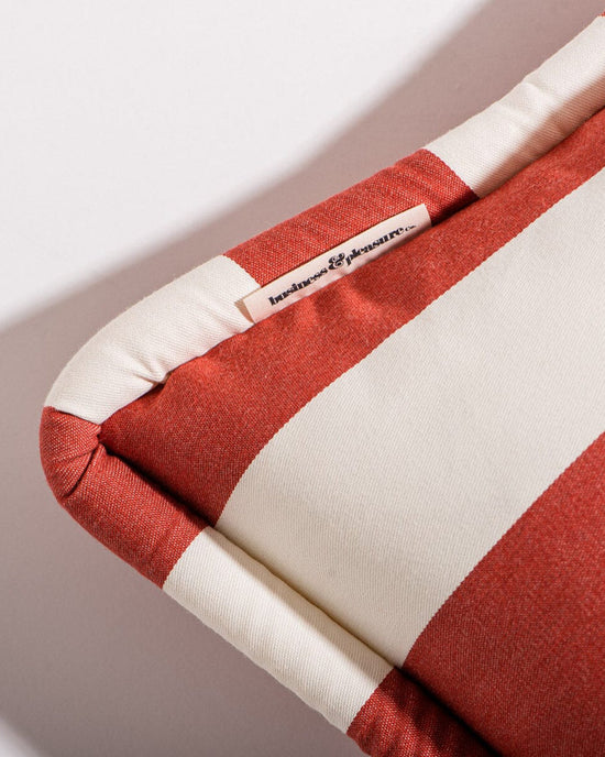 Close-up of the Small Square Throw Pillow - Crew Le Sirenuse Stripe by Business & Pleasure Co, featuring red and white stripes and a sewn-in “leisure & pleasure” label, angled on a white background—ideal for indoor-outdoor pillow collections.