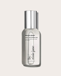 A clear 3 fl oz (115 ml) bottle of Rosie Jane Beach Baby Body + Hair Perfume Mist with a silver cap sits against a light beige background. The bottle displays black text and is ideal for both body and hair.