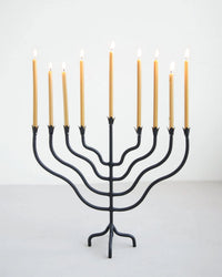 The Floral Society's Beacon Menorah - Tall, featuring nine glowing gold Hanukkah candles, stands on a light gray surface against a plain white background.