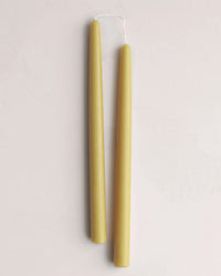 Two 12in Beeswax Taper Candles by The Floral Society, joined at the wick, are displayed side by side on a pale, neutral background.