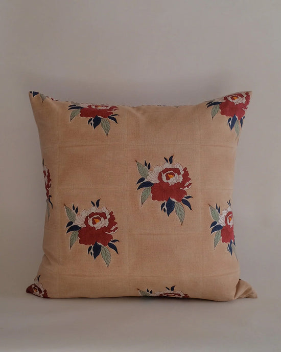 The Babita Linen Pillow (22x22 in Red) from Soil to Studio features a beige background with red and pink floral patterns and green leaves, inspired by the Valley of Flowers, shown against a simple, light backdrop.