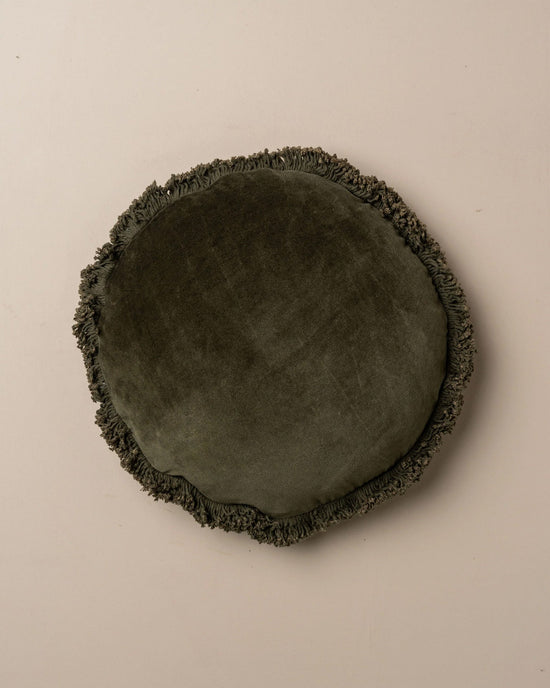 The Saarde Velvet Round Pillow w/ Feather Insert in Dark Olive features a fringed edge and round shape, shown against a plain light background.