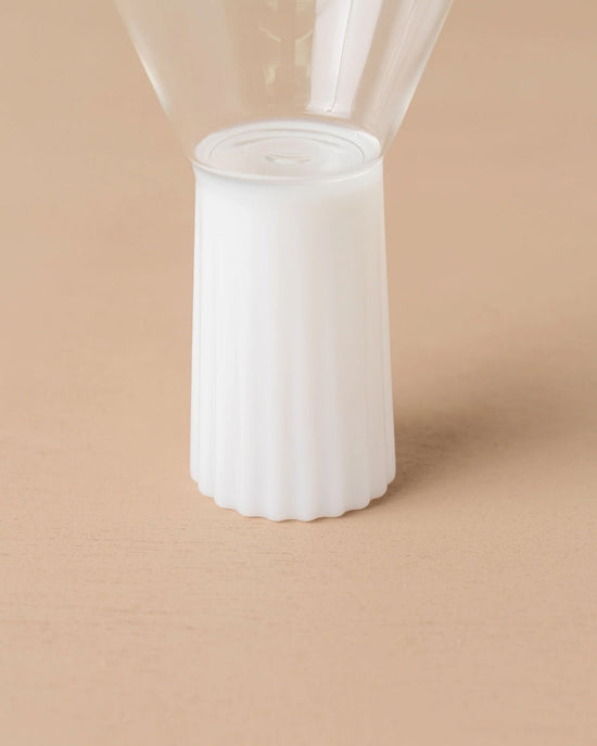 Close-up of the base of the Saarde Kairos Wine Glass in Opaque White, featuring a ribbed cylindrical stand, set on a light beige surface.