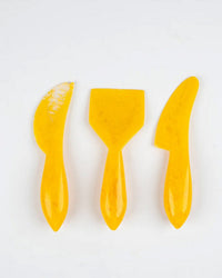 The Casa Amarosa Resin Cheese Knife Set of 3 in Yellow features uniquely shaped blades, arranged vertically on a white background—an ideal, stylish addition to your charcuterie board collection.