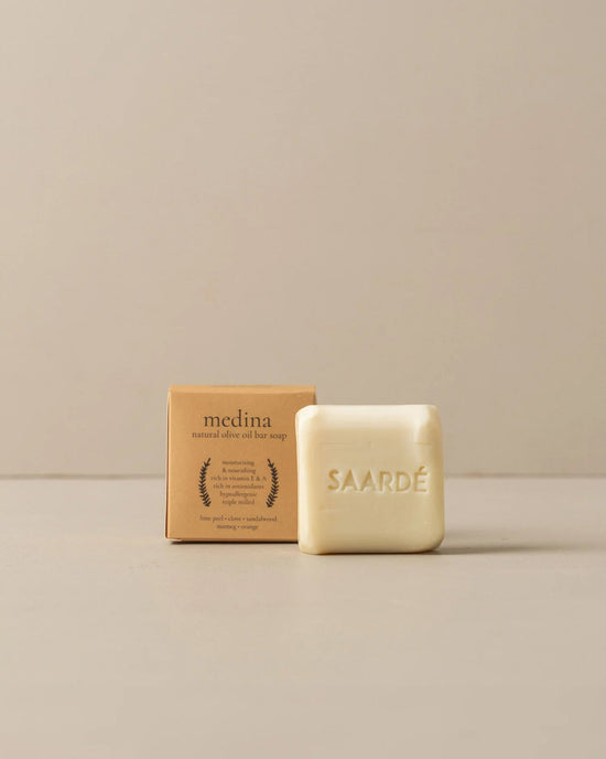 A moisturizing Saarde Olive Oil Bar Soap in Medina is embossed with the brand’s name and placed in front of a brown box labeled medina natural olive oil bar soap.