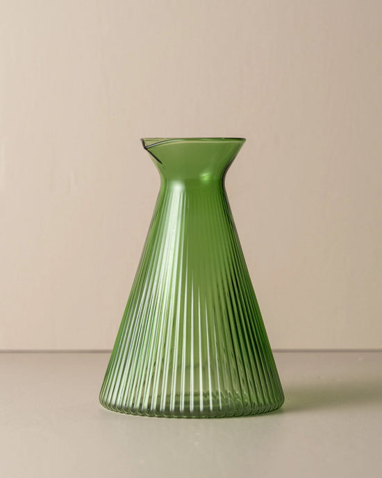 The Saarde Kairos Angular Carafe in Green, featuring a ribbed conical design and crafted from borosilicate glass, is set against a plain beige background.
