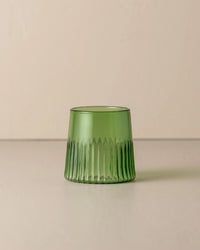 The Saarde Kairos Medium Water Glass in Green, with vertical ribbed texture, rests on a neutral surface against a beige background.