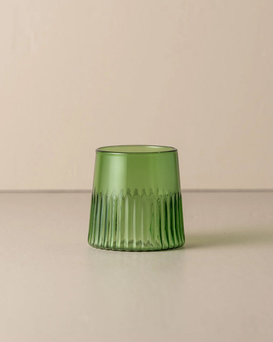 The Saarde Kairos Medium Water Glass in Green, with vertical ribbed texture, rests on a neutral surface against a beige background.