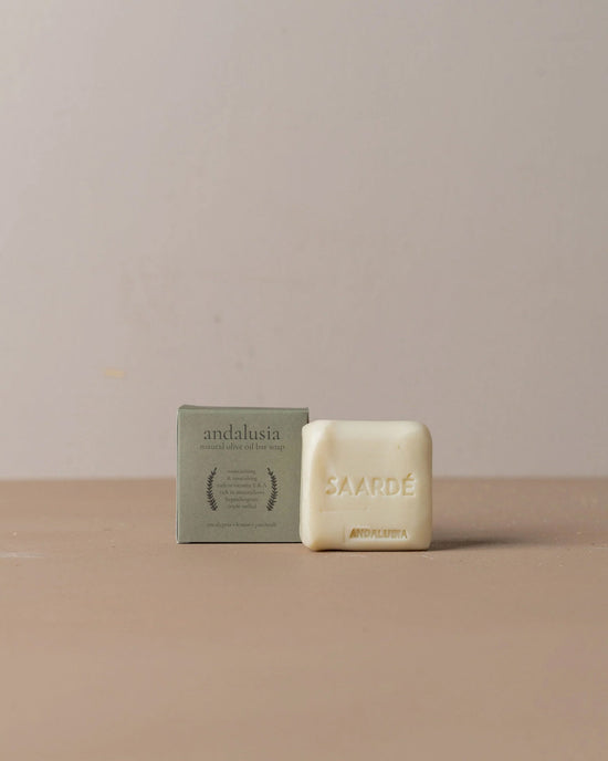 A bar of Saarde Olive Oil Bar Soap in Andalusia sits beside its green cardboard packaging on a plain beige surface with a light background.