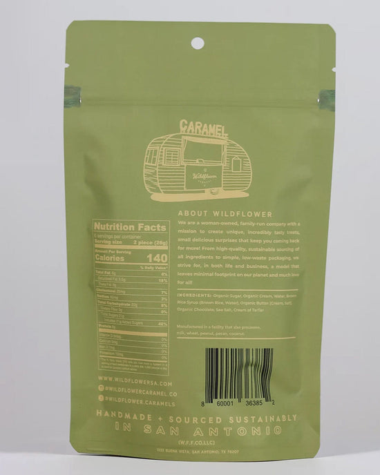 The back of a green Wildflower Caramel Co Dark Chocolate Sea Salt Caramels in A Bag shows nutritional facts, ingredients, company info, barcode, and states the product is handmade and sustainably sourced in San Antonio, TX with fair trade caramels.