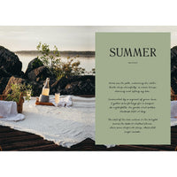 A picnic on a lakeside deck features a white blanket, carafe, glasses, and bread—capturing the charm of cabin recipes from "Four Seasons of Cabin Cooking" by Cozy Publishing. Calm water and nature complete the inviting summer scene.