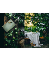 A split image: on the left, green apples, leaves, a striped notebook, and candle; on the right, an elegant garden table inspired by Nordic summer recipes from the Nordic Summer Cookbook by Cozy Publishing.