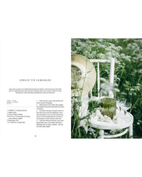 A white chair in a field holds a straw hat, a jar of spruce tip lemonade, and small white flowers; the Nordic Summer Cookbook by Cozy Publishing features the recipe text on the left, evoking a serene midsummer table scene.