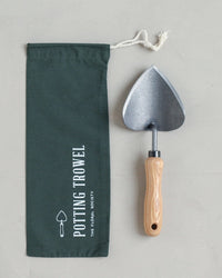 The Floral Society Potting Trowel, featuring a sturdy metal design and wooden handle, is shown next to a dark green drawstring bag with a trowel graphic—a must-have garden tool for every collection.