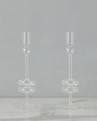The etúHOME Clear Glass Candlesticks Set of 2 - Medium features handmade recycled glass holders with rounded accents, shown on a white marble surface against a plain gray background.