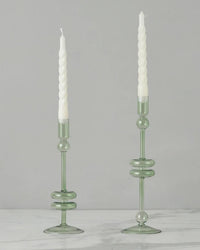 Two Sage Glass Candlesticks Set of 2 - Medium by etúHOME, handmade from recycled glass, hold white twisted candles on a white marble surface against a plain light gray background.