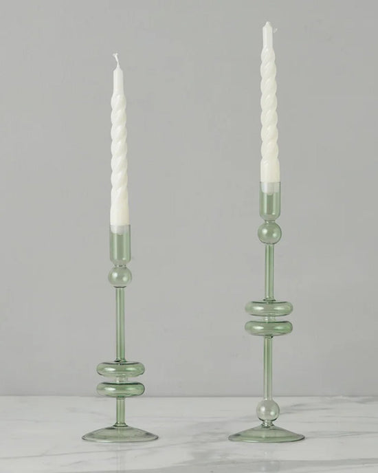 Two Sage Glass Candlesticks Set of 2 - Medium by etúHOME, handmade from recycled glass, hold white twisted candles on a white marble surface against a plain light gray background.