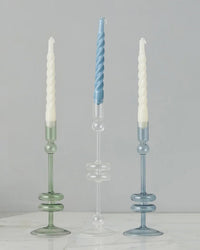 Two Sage Glass Candlesticks by etúHOME, handmade from recycled glass, are displayed on a white marble surface against a gray background. This elegant set of medium taper candle holders adds timeless charm to any décor.