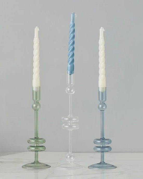 Two Sage Glass Candlesticks by etúHOME, handmade from recycled glass, are displayed on a white marble surface against a gray background. This elegant set of medium taper candle holders adds timeless charm to any décor.