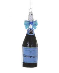 The Cody Foster Champagne With Bow- Blue Ornament is a glass decoration shaped like a champagne bottle, featuring a blue label and matching bow, and hangs by a silver string for a festive touch to your tree.