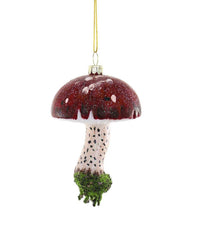 The Cody Foster Enchanted Forest Toadstool Ornament is a hand-crafted glass Christmas tree ornament shaped like a red and white glittery mushroom, with black-spotted white stem, green moss base, and gold hanging string.