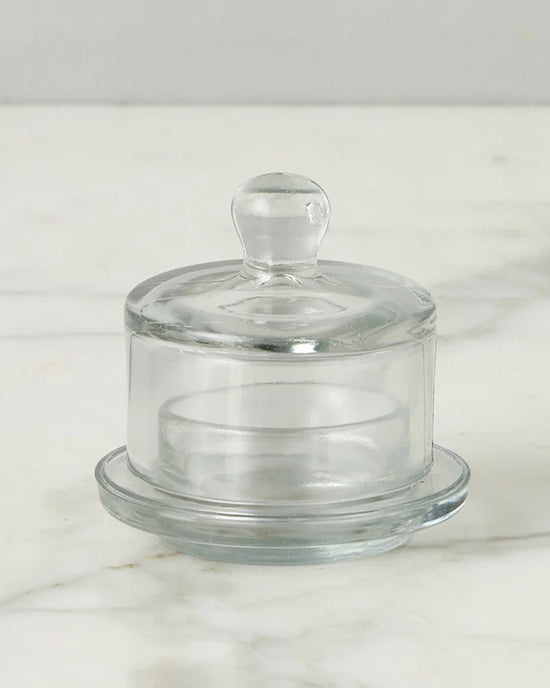 The etúHOME Bistro Glass Jam Jar, Round, features a clear glass design with a knob handle lid, reminiscent of vintage style, and is shown on a white marble surface.