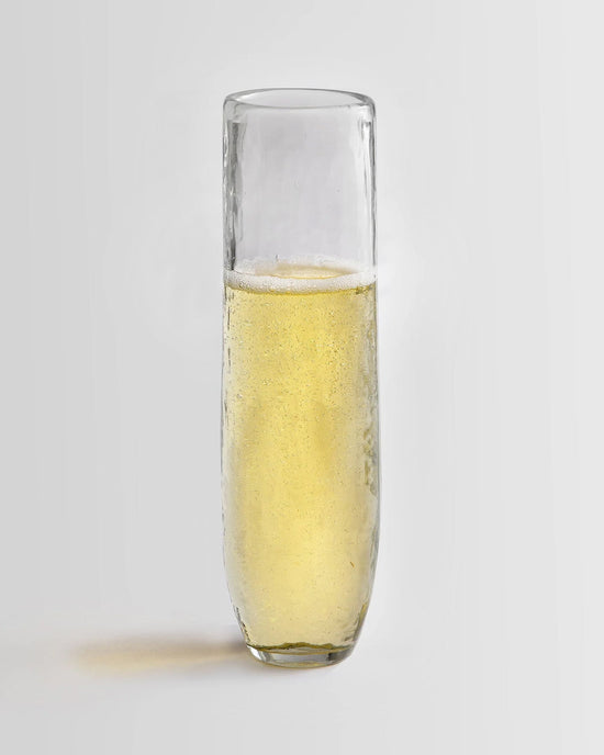 A Pebbled Stemless Flute from The Collective, filled with a light yellow, carbonated drink, is displayed against a plain white background.