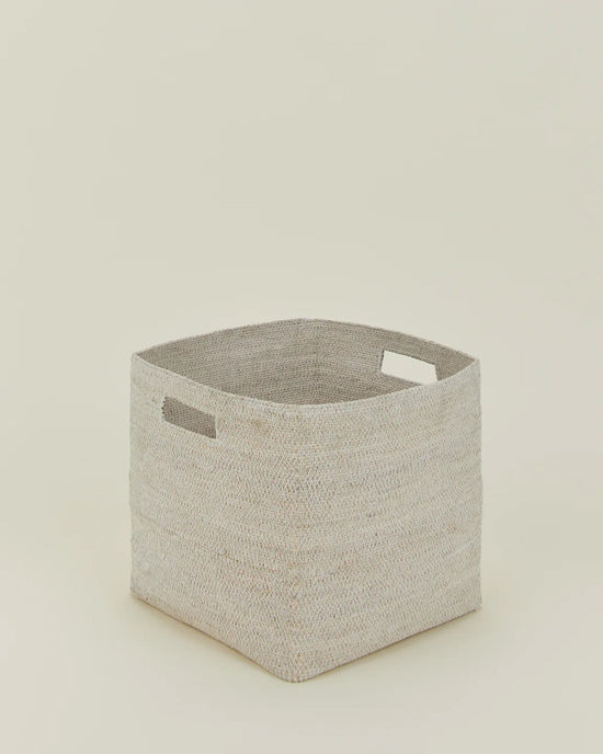 The Hawkins New York Essential Woven Storage - Square Basket in light beige seagrass features two rectangular cutout handles and is shown on a plain, off-white background.