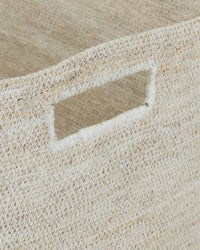 Close-up of the Essential Woven Storage - Low Basket by Hawkins New York, featuring a rectangular cut-out handle. The natural seagrass fibers and tight weave make it ideal for storing blankets or organizing your pantry.