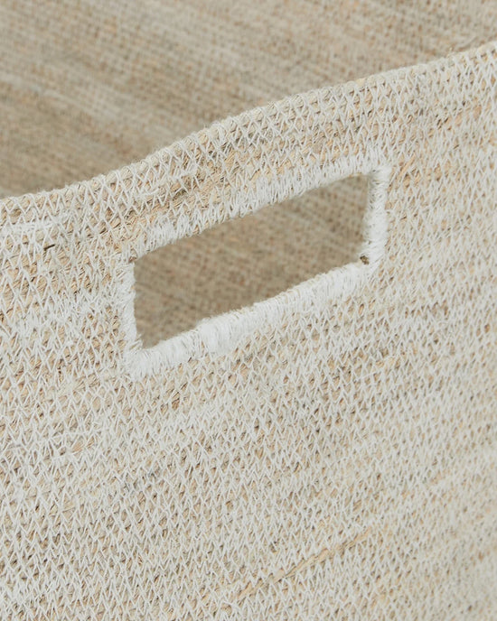 Close-up of the Essential Woven Storage - Low Basket by Hawkins New York, featuring a rectangular cut-out handle. The natural seagrass fibers and tight weave make it ideal for storing blankets or organizing your pantry.