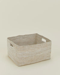 The Hawkins New York Essential Woven Storage - Low Basket is a rectangular seagrass basket with cutout handles and a natural beige tone, ideal for organizing your pantry or storing blankets. Shown on a neutral, light background.