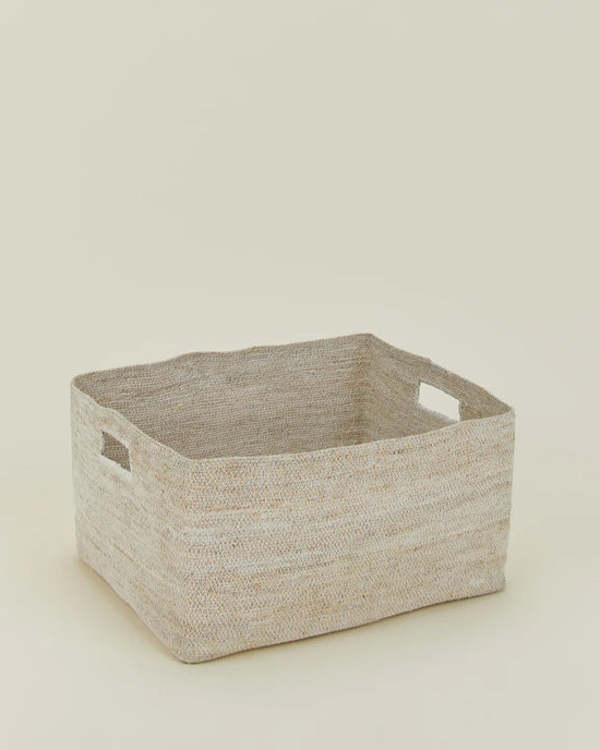 The Hawkins New York Essential Woven Storage - Low Basket is a rectangular seagrass basket with cutout handles and a natural beige tone, ideal for organizing your pantry or storing blankets. Shown on a neutral, light background.